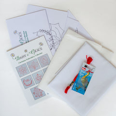 Christmas embroidery collection kit displayed with instructions, patterns, white cotton fabric, embroidery floss, and needles.